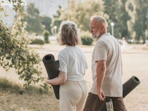 Pareja de personas mayores camina por el parque con esterillas de yoga, disfrutando del estilo de vida activo y consciente que aporta la meditación en personas mayores