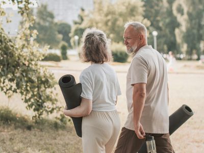 Pareja de personas mayores camina por el parque con esterillas de yoga, disfrutando del estilo de vida activo y consciente que aporta la meditación en personas mayores