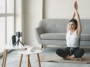 Mujer practicando Hatha Yoga en clases online desde casa con cámara en trípode.