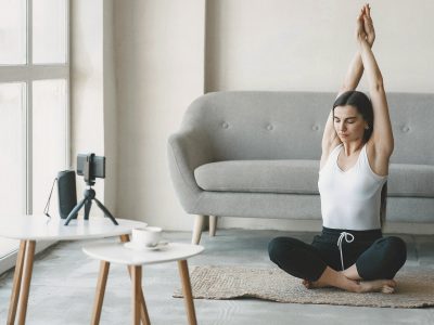 Mujer practicando yoga online desde casa con cámara en trípode.
