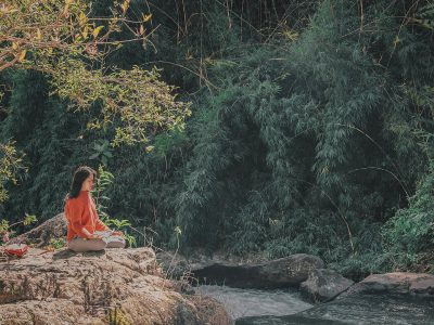 Confusión sobre el yoga: mujer meditando sentada en la naturaleza junto a un río, simbolizando el sentido interior del yoga.