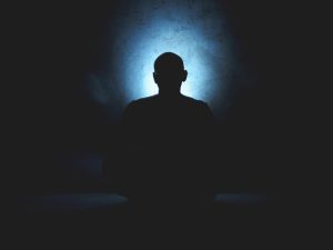 Silueta de una persona meditando en la oscuridad, representando el aislamiento sensorial del Bhramari Pranayama.