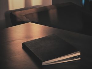 Agenda de cuero sobre mesa de madera en penumbra para consultas de reestructuración personal y mentoría de 8 semanas. Físico y Mental.